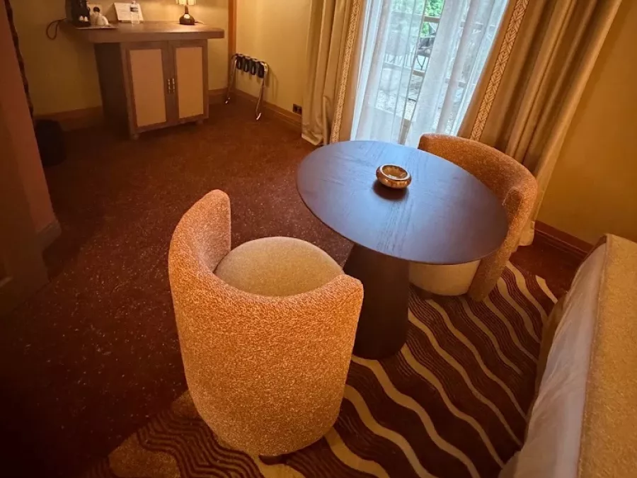 Coin salon de la chambre : table ronde, deux fauteuils en bouclette et rideaux à galon
