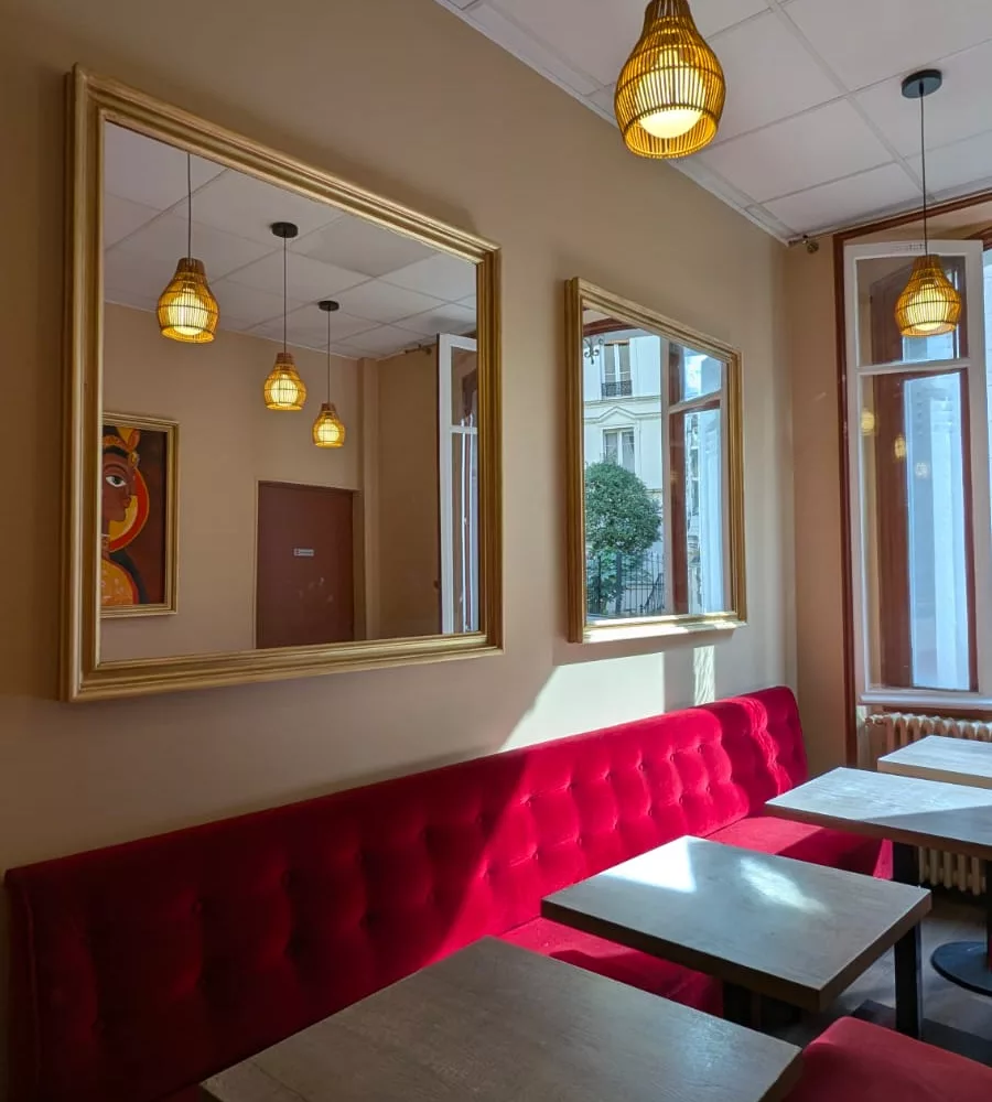 Salle du restaurant RANI à Paris : banquette capitonnée, miroirs dorés et suspensions en rotin